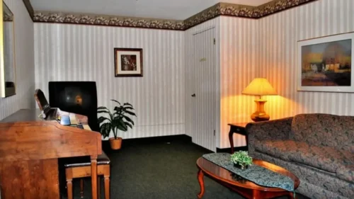 A sitting room with striped wallpaper, a couch with a floral pattern, a television, and a wooden side table with a lamp
